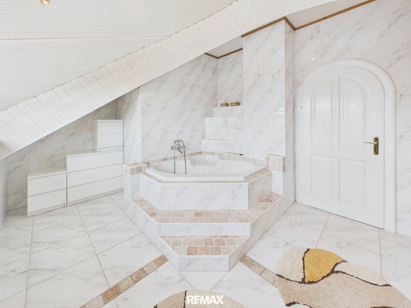 Geräumiges Badezimmer mit Eckbadewanne, Marmorfliesen und Dachschräge.