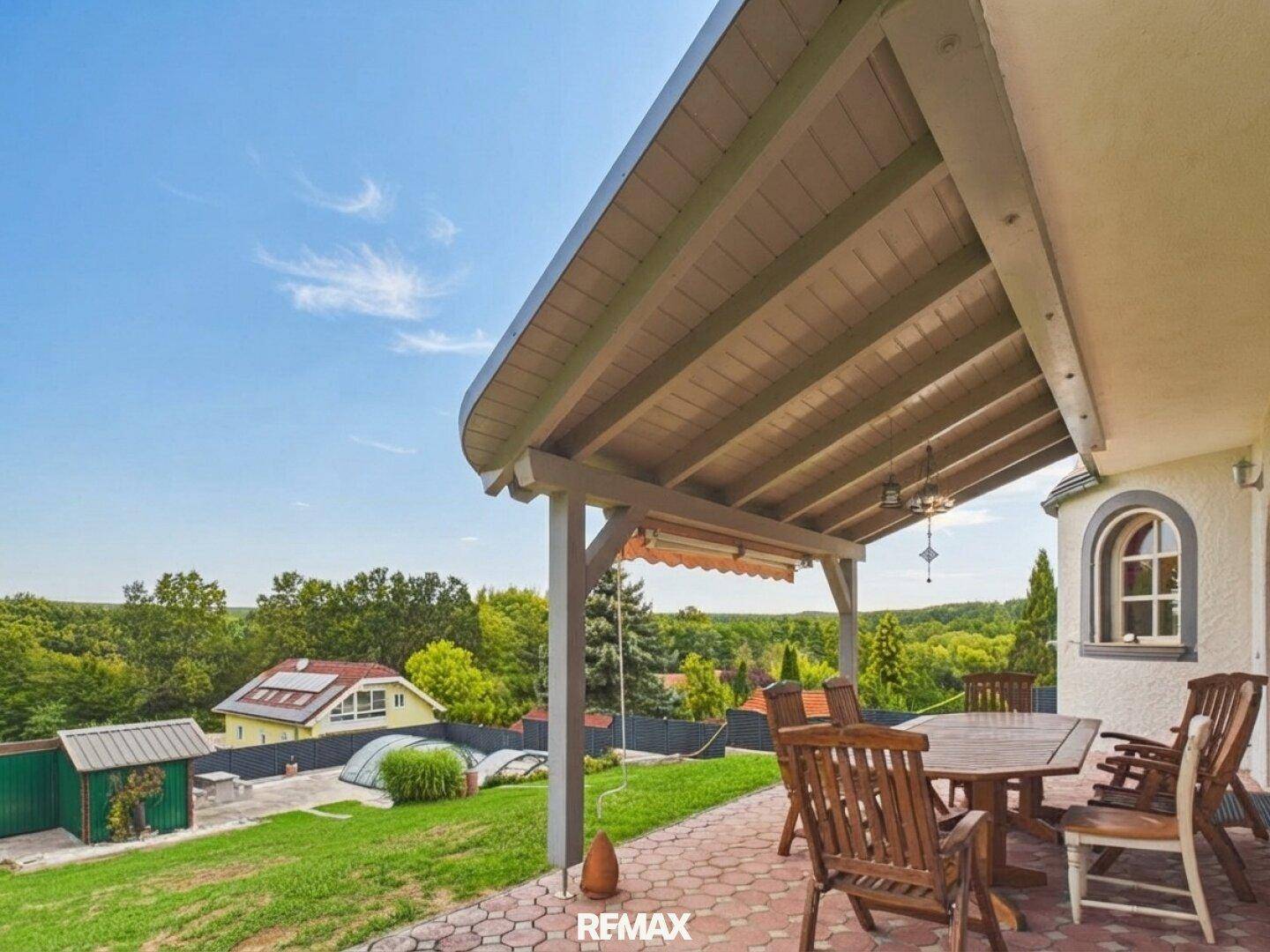 Überdachte Terrasse mit Holztisch, Stühlen und weitem Blick über die Landschaft.