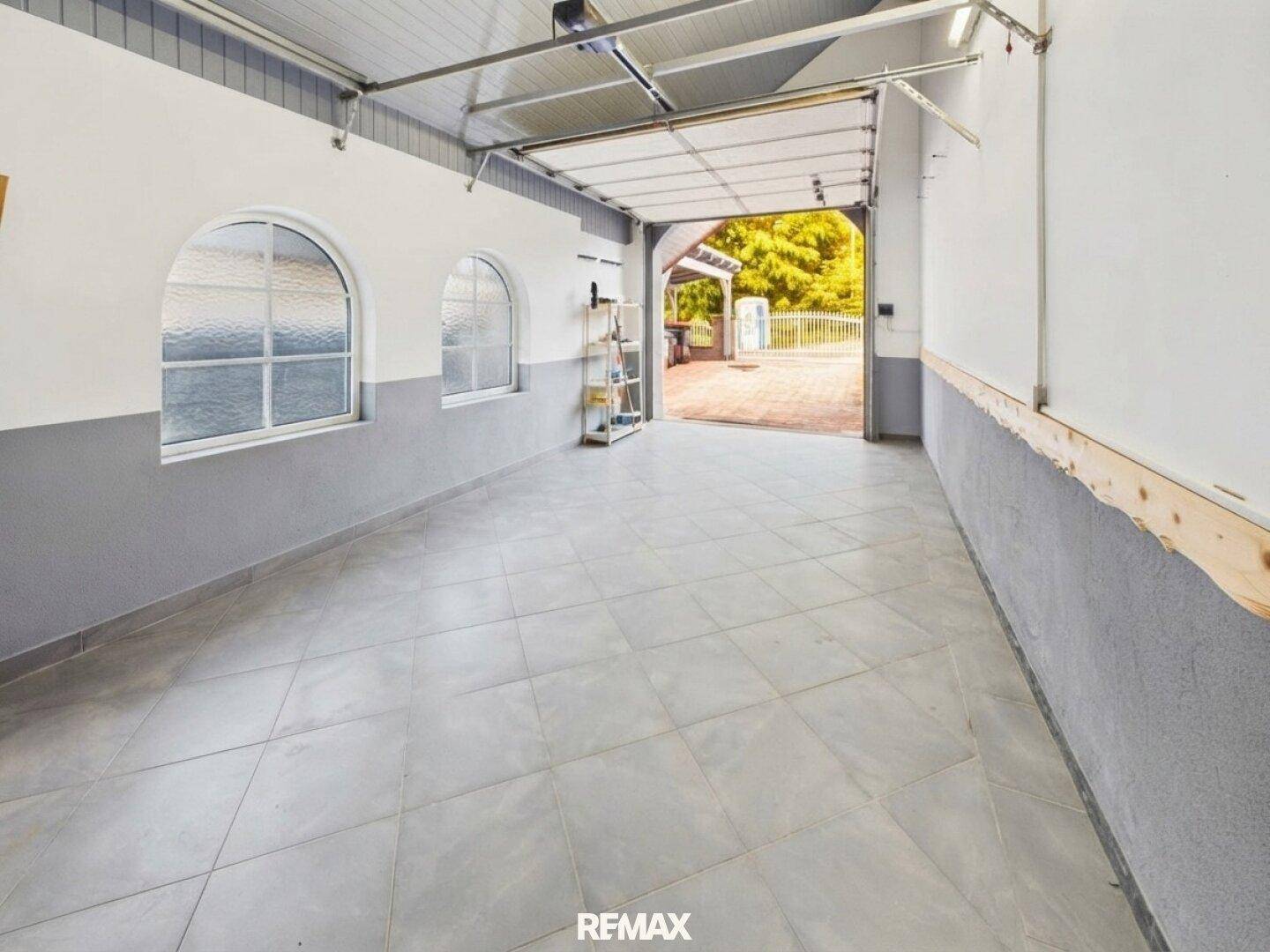 Geräumige Garage mit Fliesenboden, Fenstern und direktem Zugang nach draußen.