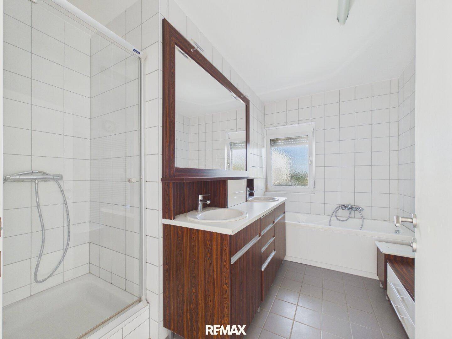 Modernes Badezimmer mit weißen Fliesen, Dusche, Badewanne, Doppelwaschbecken und Fenster.