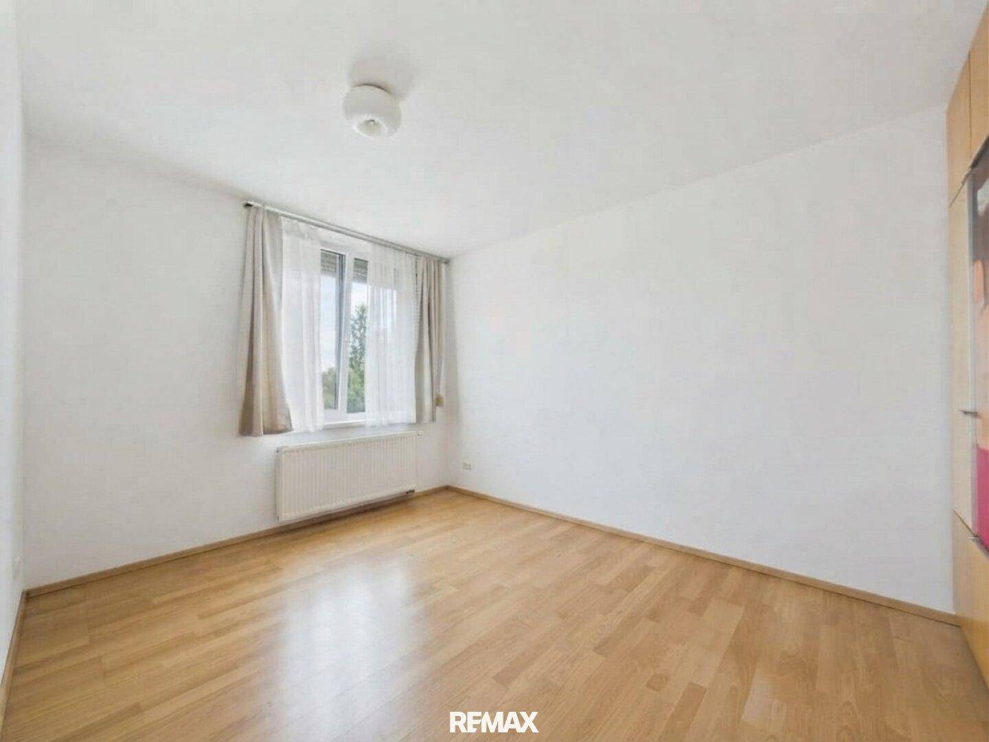 Ruhiges Zimmer mit Parkettboden und Fenster, das viel Tageslicht in den Raum lässt.
