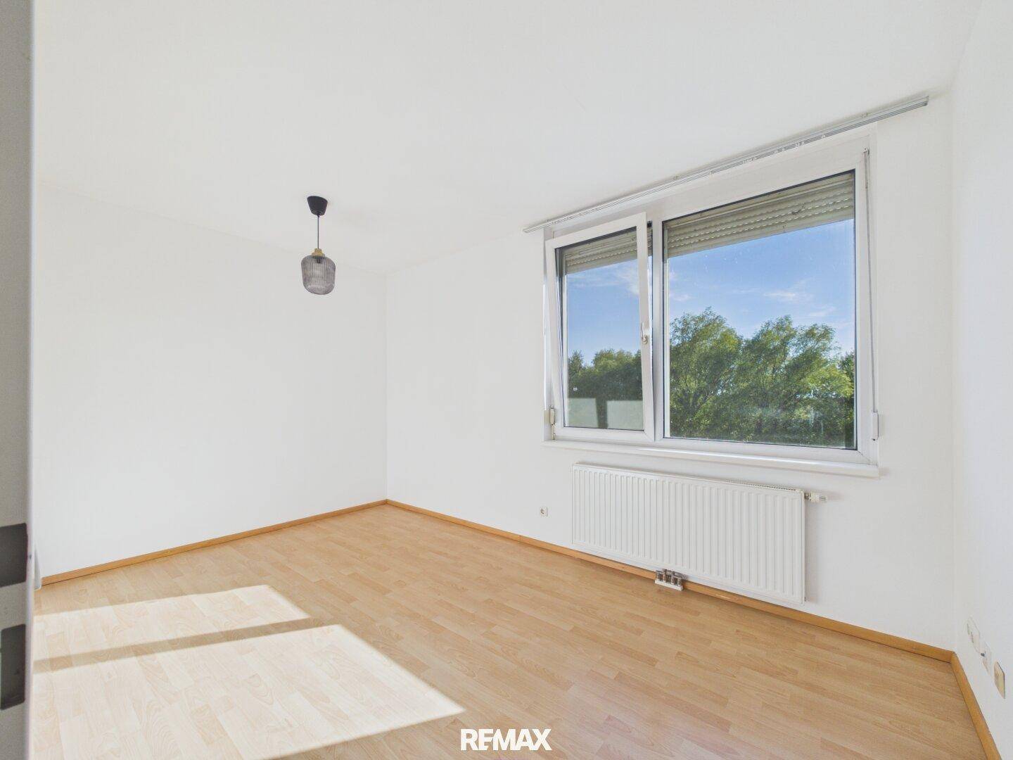 Helles Zimmer mit Parkettboden und großem Fenster, das einen schönen Blick ins Grüne bietet.