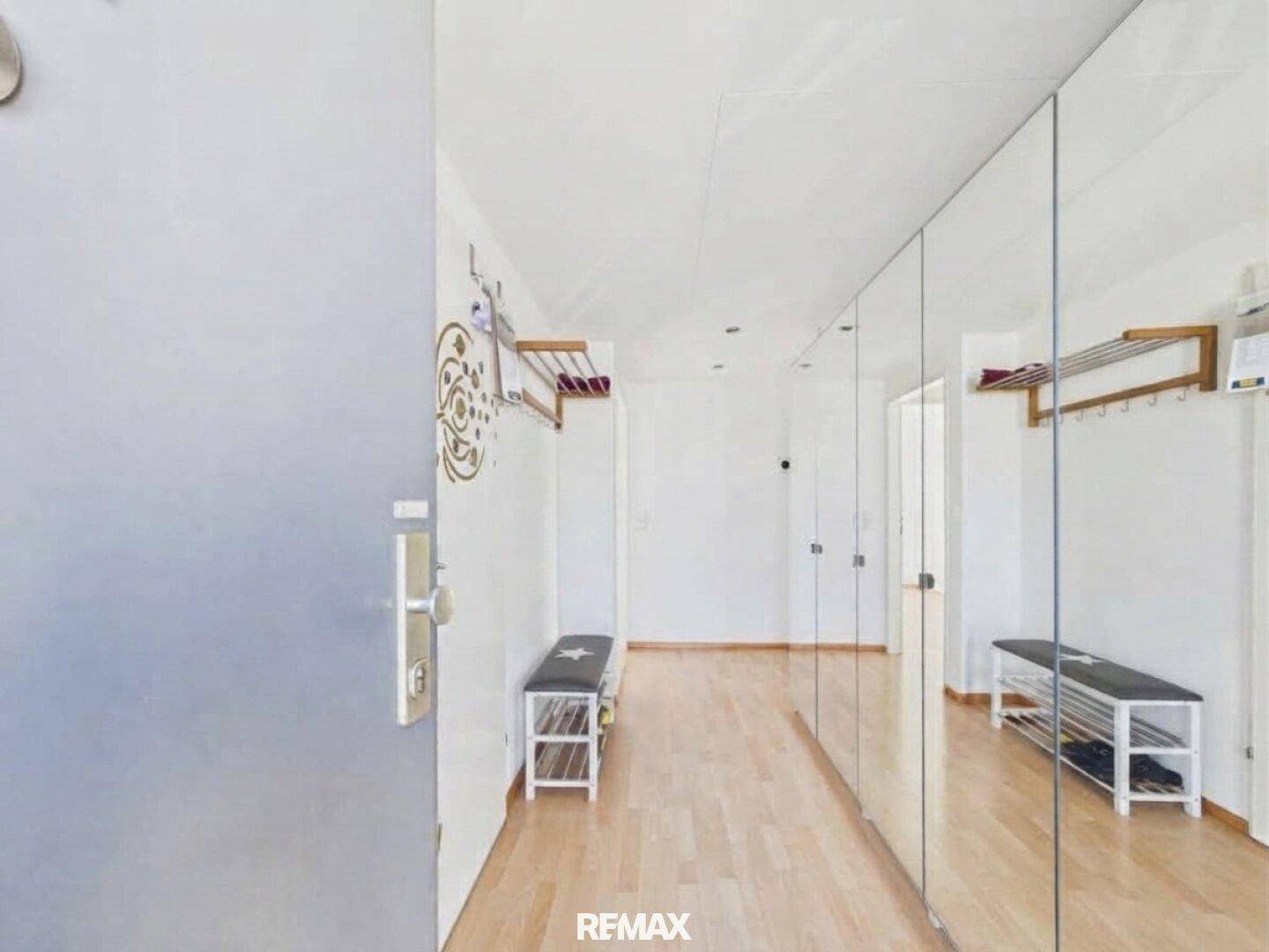 Heller Eingangsbereich mit Parkettboden, großer Spiegelwand und praktischer Garderobe.
