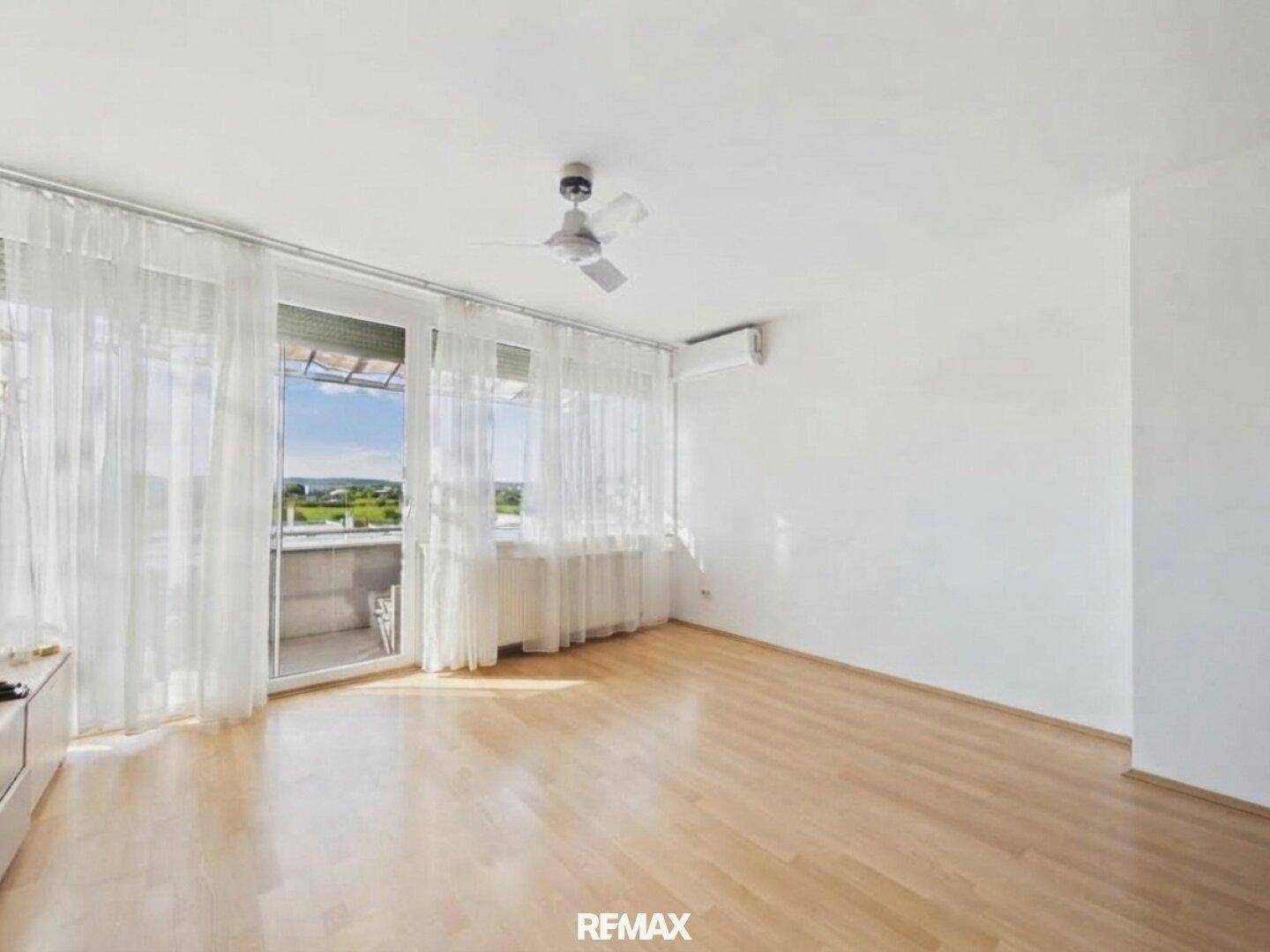Geräumiges, helles Wohnzimmer mit Parkettboden, Klimaanlage und Zugang zu einem sonnigen Balkon.