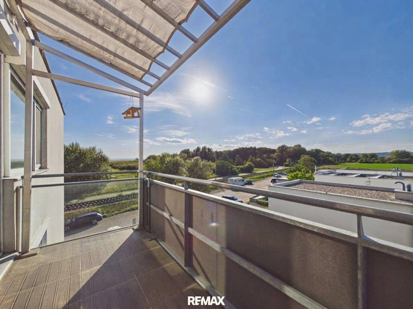 Sonniger Balkon mit Holzboden und Markise, bietet einen weiten Blick über die grüne Landschaft.