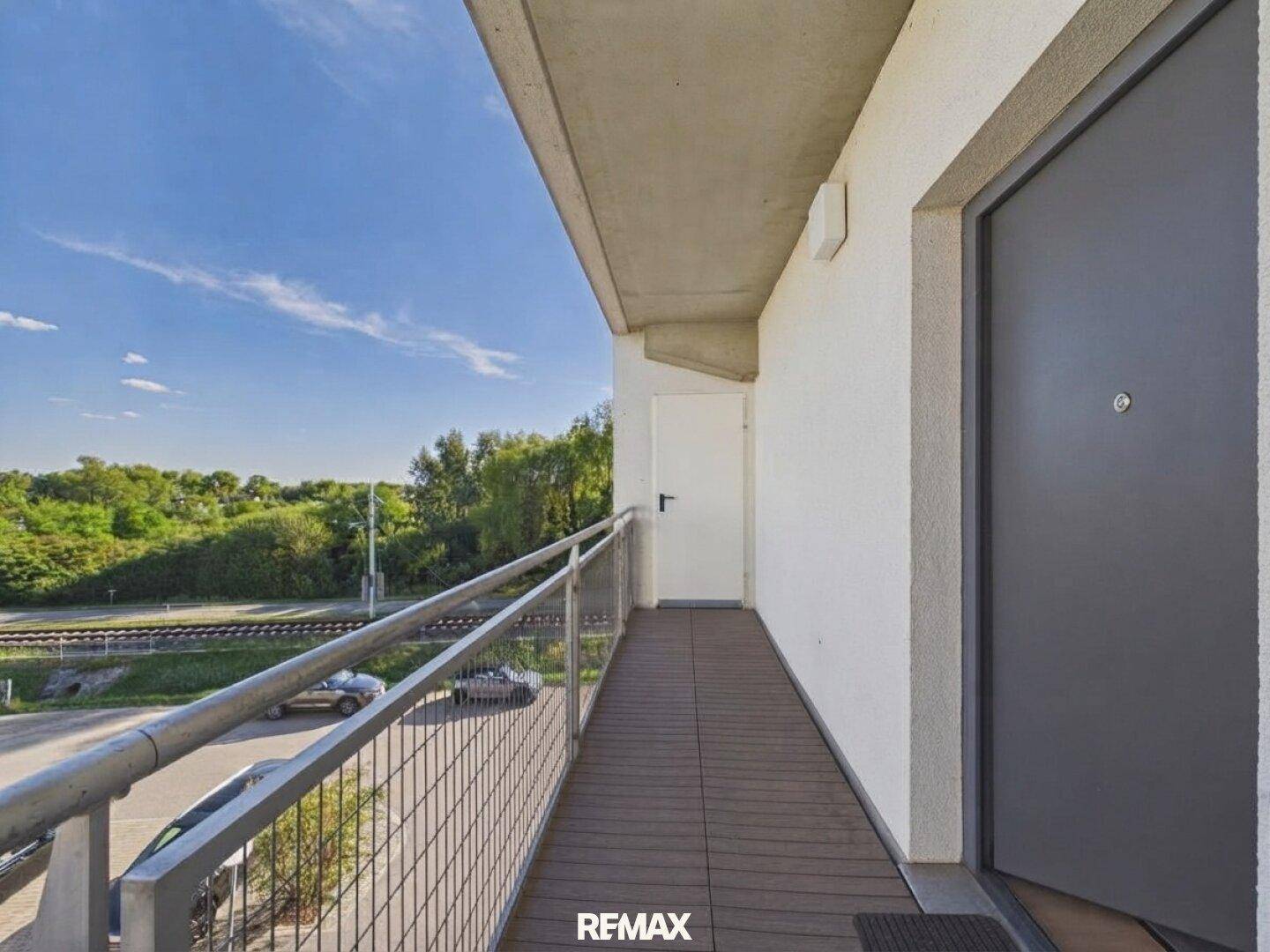 Langer Balkon mit Holzboden und Metallgeländer, bietet einen Blick auf die Umgebung und viel Grün.