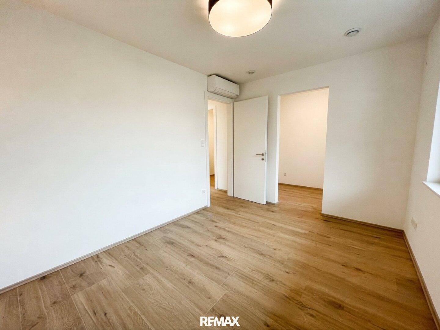Helles Schlafzimmer mit Holz-Look-Boden, Klimaanlage und Zugang zu angrenzenden Räumen.