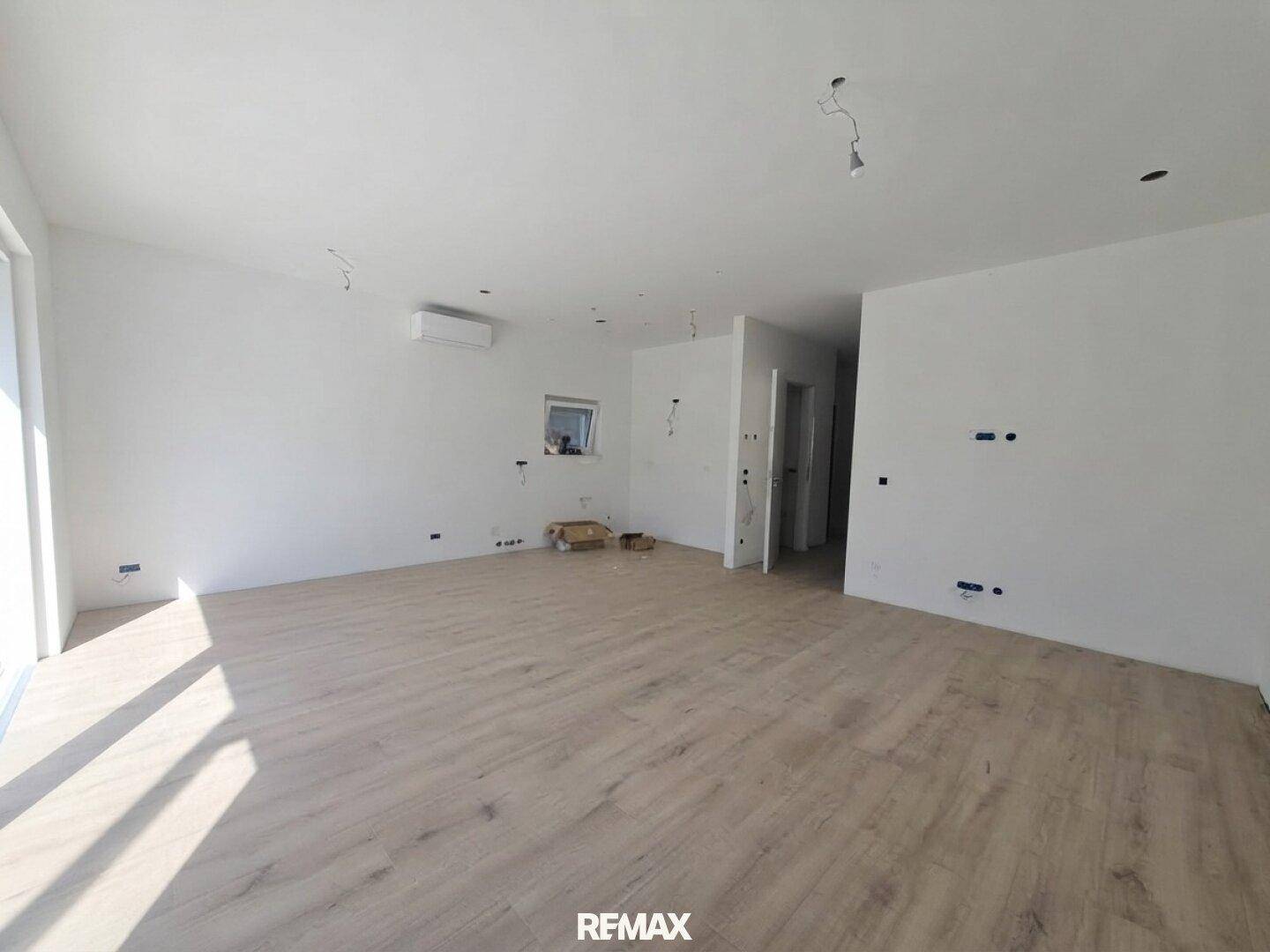 Geräumiger, heller Wohnbereich mit Holz-Look-Boden, Klimaanlage und Zugang zu weiteren Räumen.