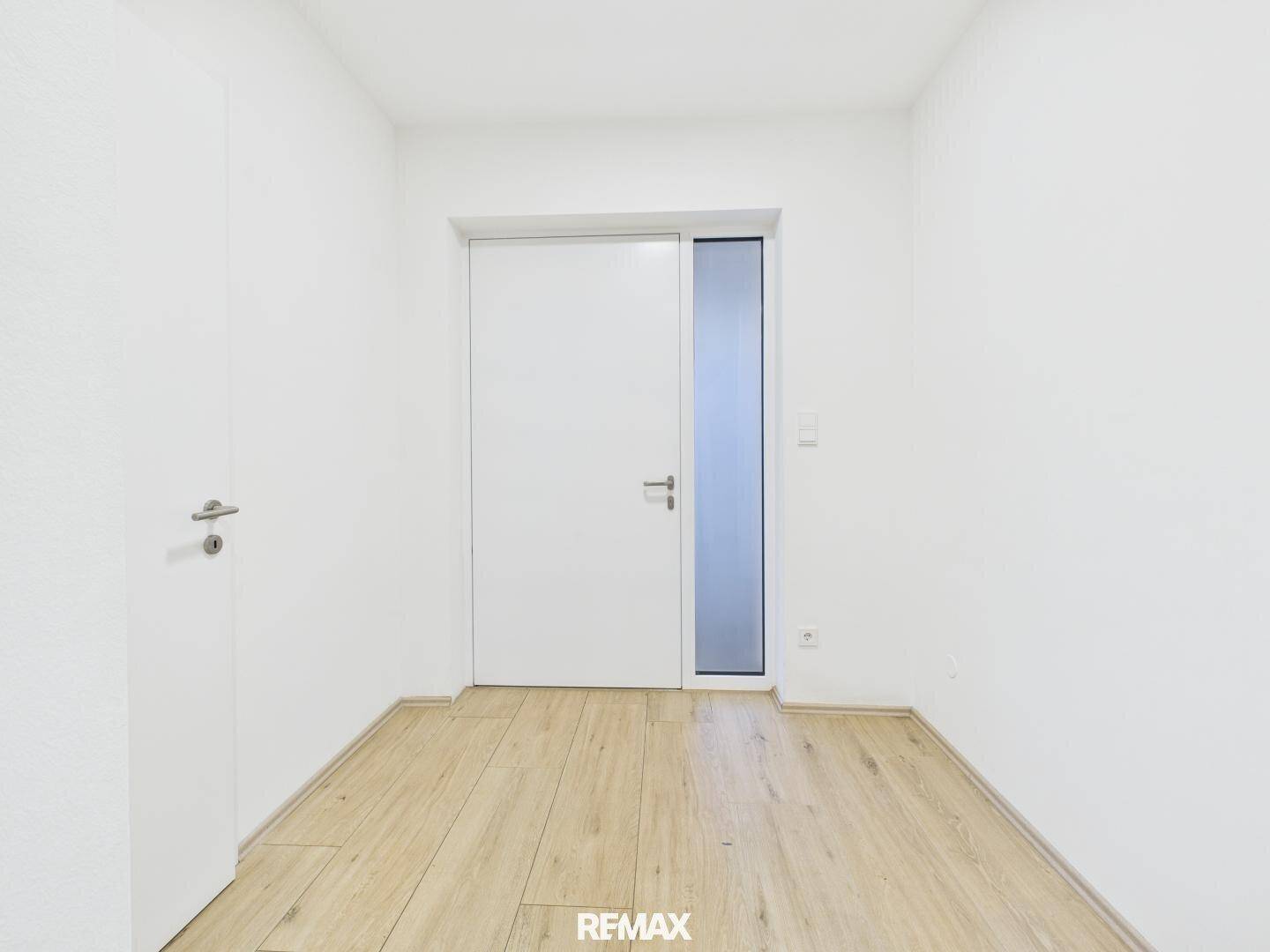 Heller Eingangsbereich mit Holz-Look-Boden und moderner weißer Tür mit Glaseinsatz.