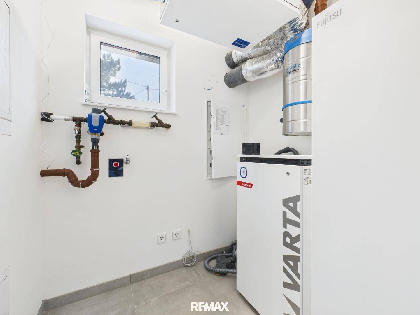 Technikraum mit moderner Wärmepumpe, Lüftungssystem und sichtbaren Installationen.