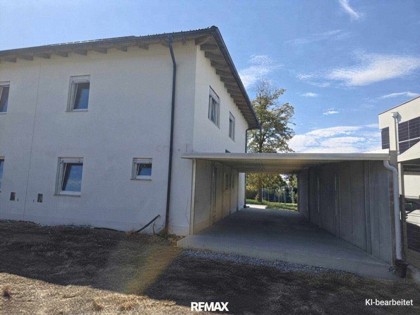 Seitenansicht des modernen Hauses mit weißer Fassade und überdachtem Carport unter klarem Himmel.