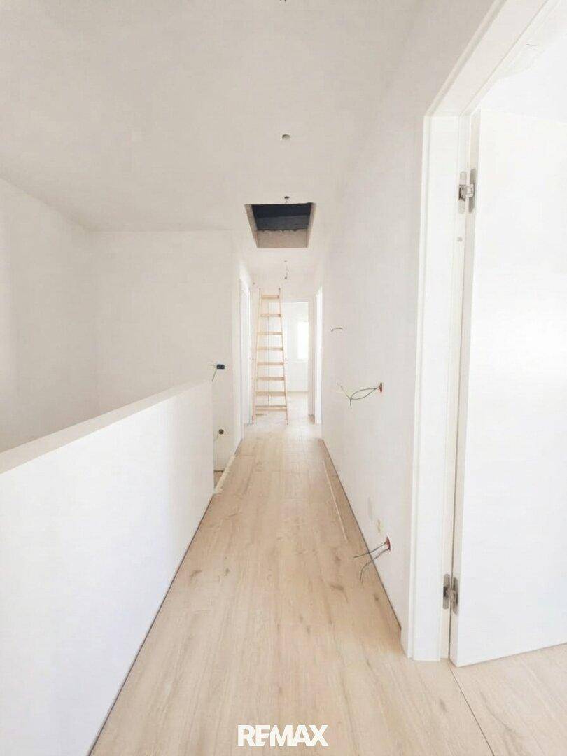 Langer, heller Flur mit Holz-Look-Boden und einer Leiter, die zu einem oberen Bereich führt.