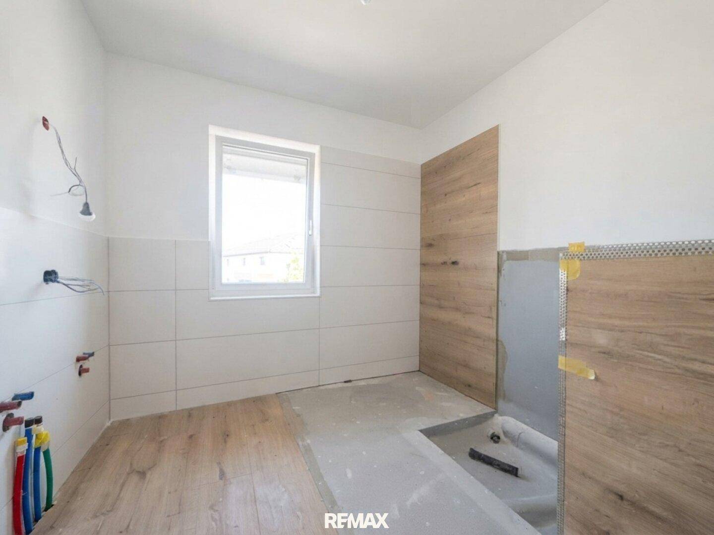 Badezimmer im Bau mit Fenster, weißen Fliesen und Holz-Look-Paneelen, bereit für die Endmontage.