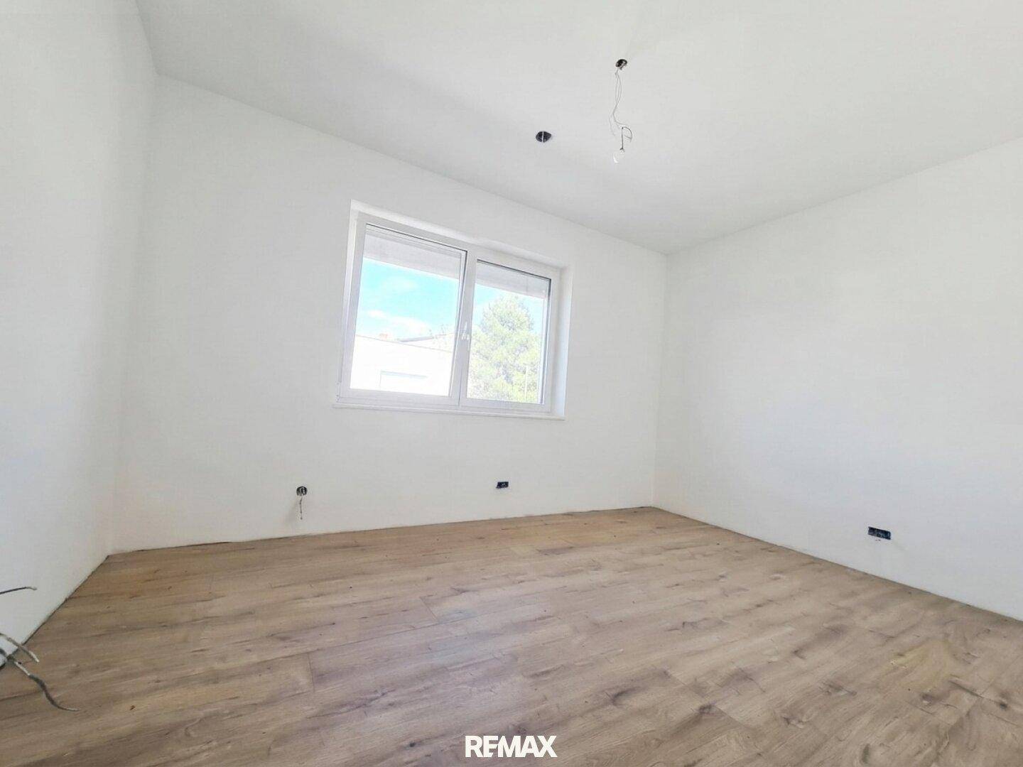 Ruhiges Schlafzimmer mit Holz-Look-Boden und einem Fenster, das viel Tageslicht hereinlässt.