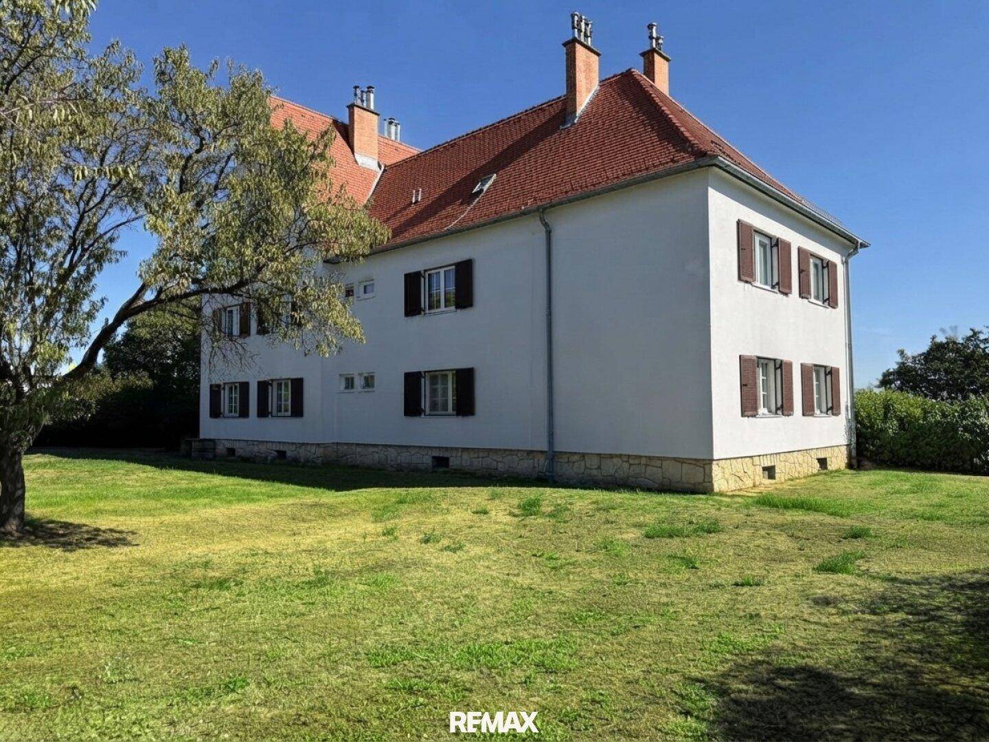 Seitenansicht eines weißen Gebäudes mit braunen Fensterläden und einem weitläufigen grünen Rasen.