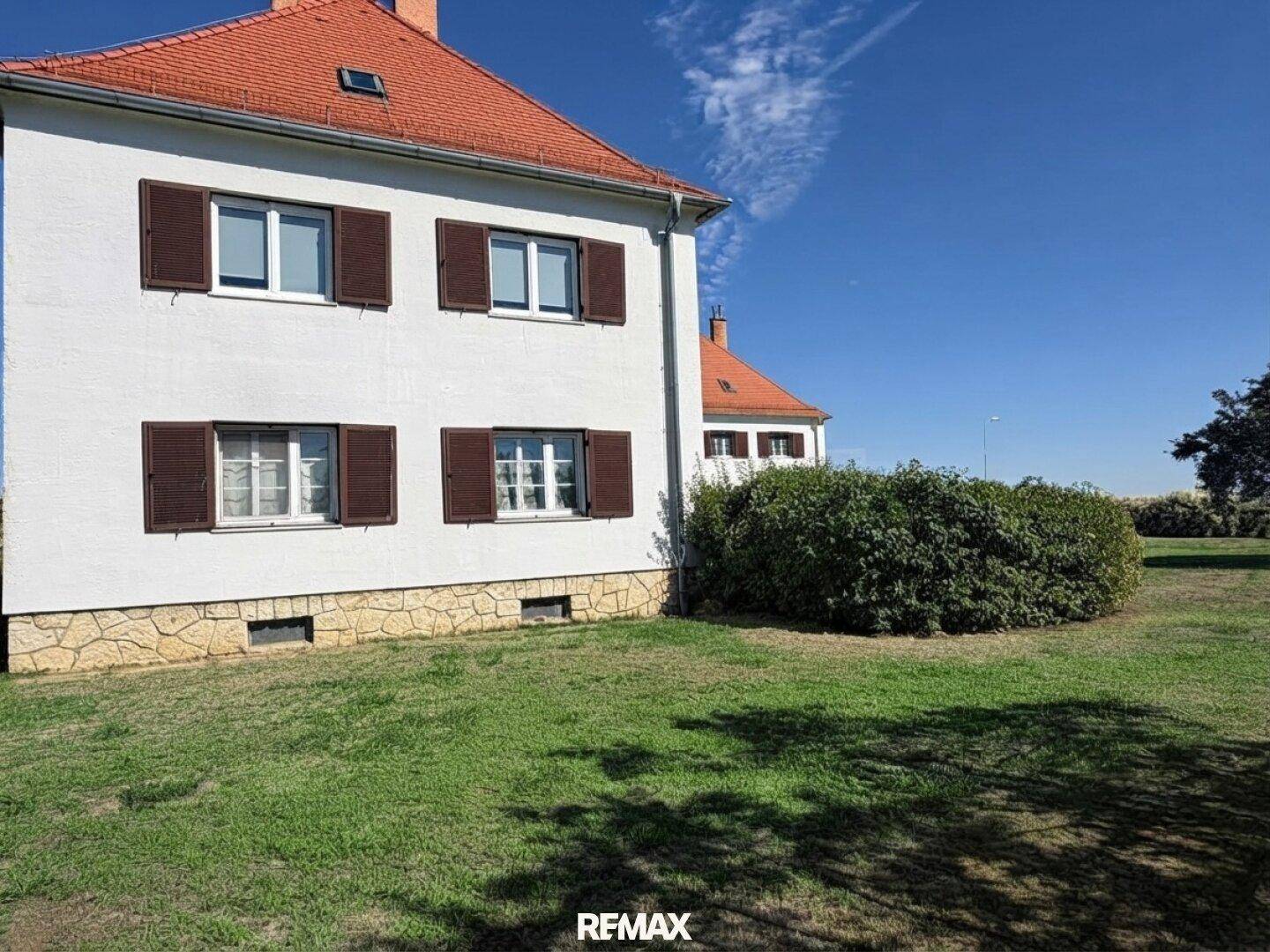Detailansicht der Gebäudeseite mit Fenstern, braunen Fensterläden und einem gepflegten grünen Rasen.