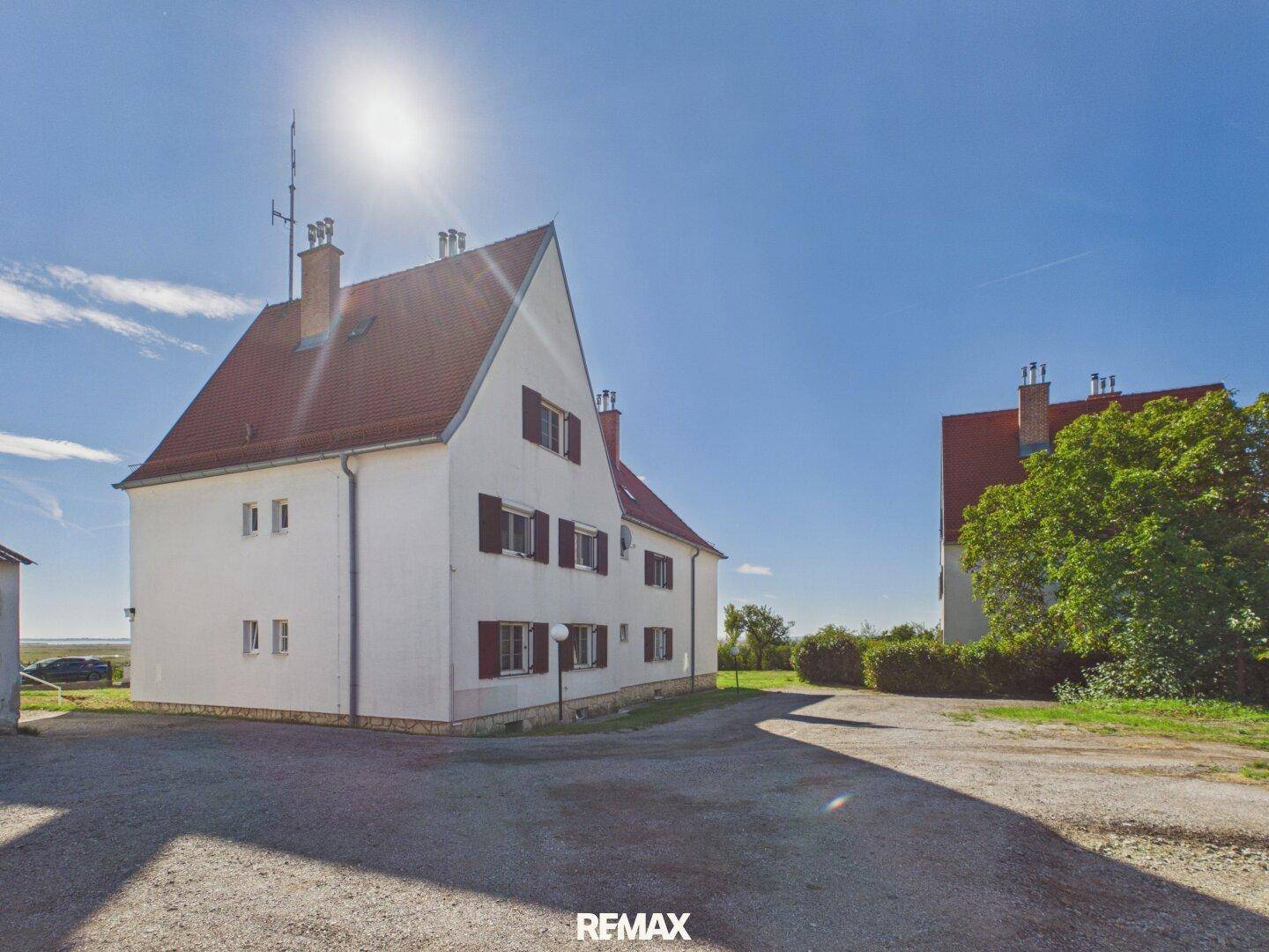 Seitenansicht eines Gebäudes mit rotem Dach und großem Kiesbereich unter strahlend blauem Himmel.