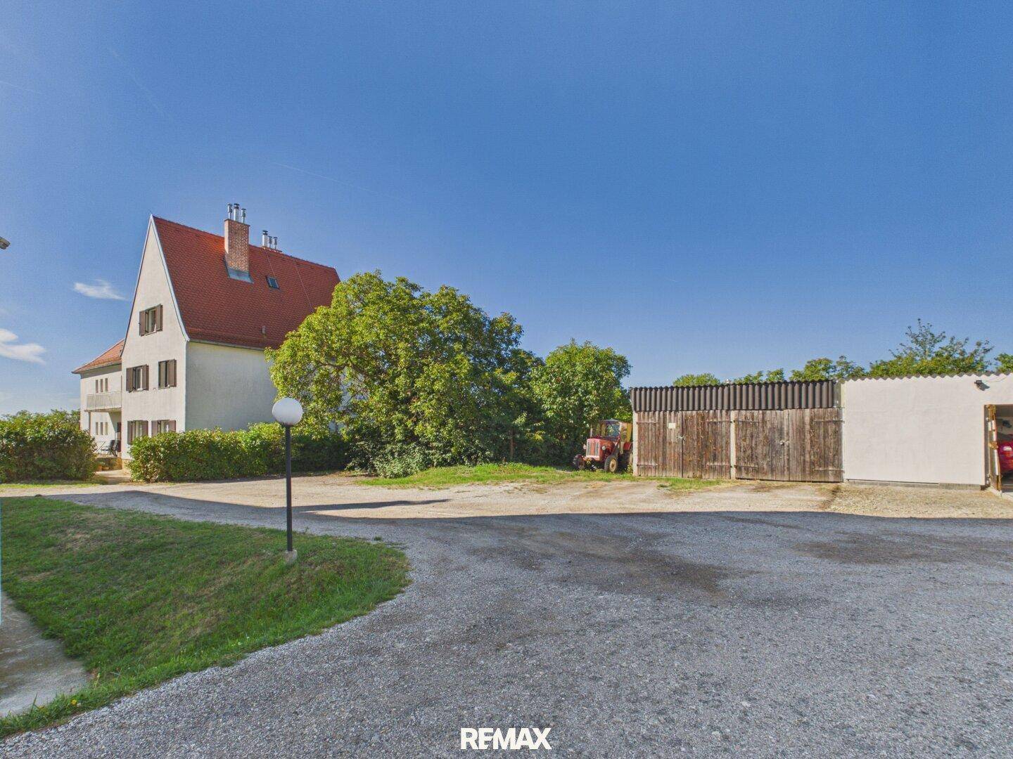 Großer Kiesbereich mit einem Schuppen und dem Hauptgebäude im Hintergrund unter blauem Himmel.