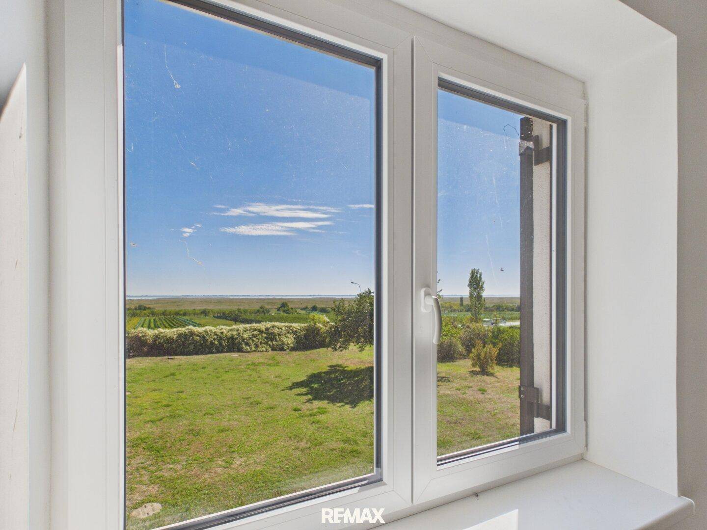 Fenster mit weitem Blick über eine grüne Landschaft und Felder unter blauem Himmel.