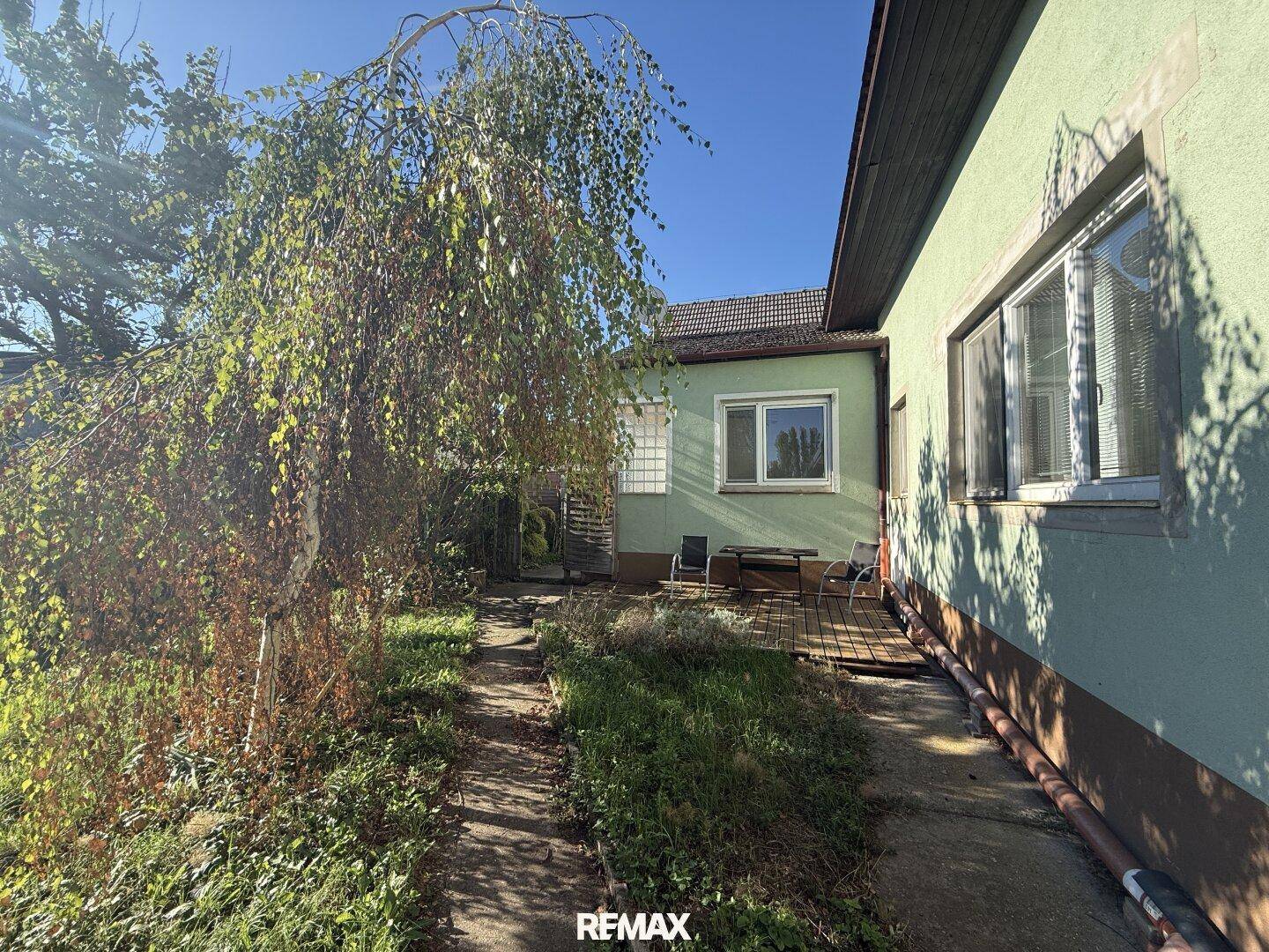 Blick in den grünen Garten mit Terrasse und Sitzgelegenheiten unter freiem Himmel.