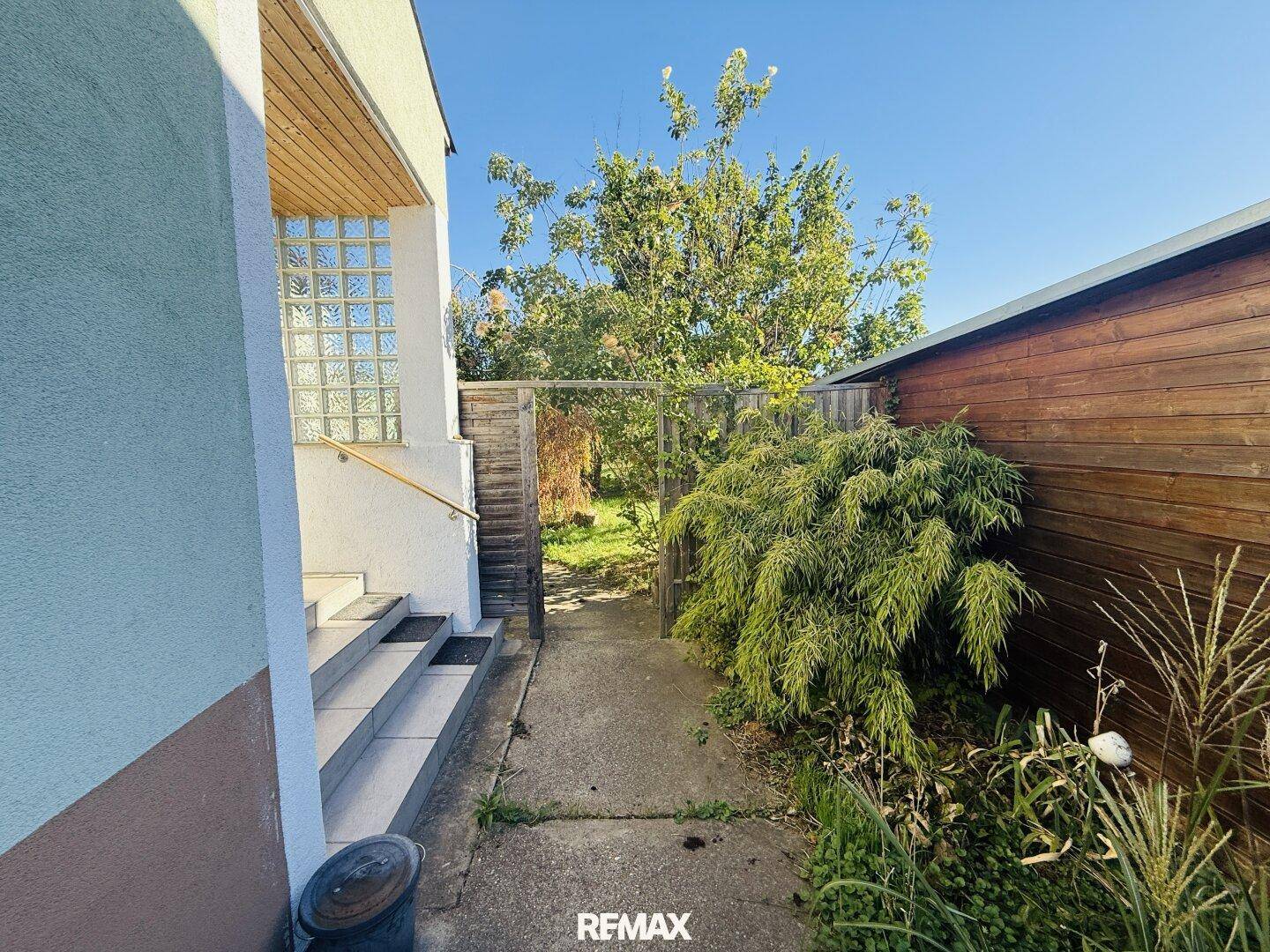 Seitlicher Zugang zum Garten mit Treppe und Holzzaun, umgeben von üppigem Grün.