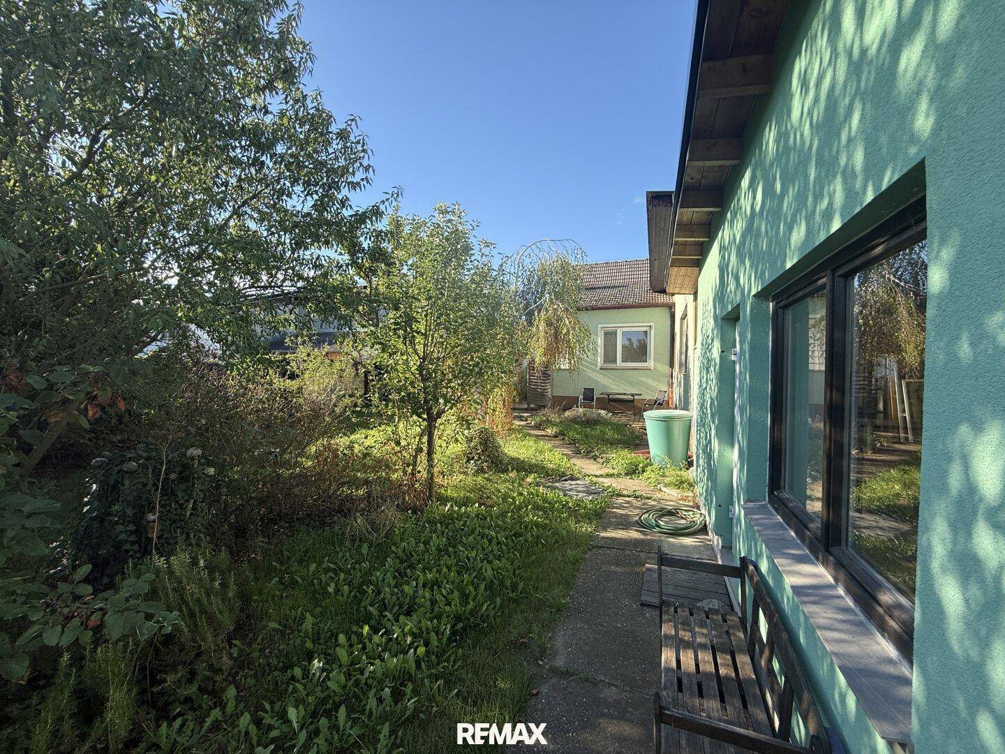 Gepflegter Gartenweg mit schattenspendenden Bäumen und einer Holzbank zum Verweilen.