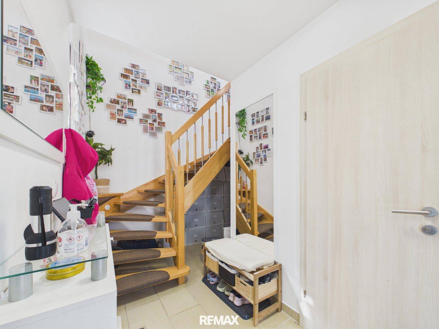 Heller Eingangsbereich mit Holztreppe, Fliesenboden und dekorativen Familienfotos an der Wand.