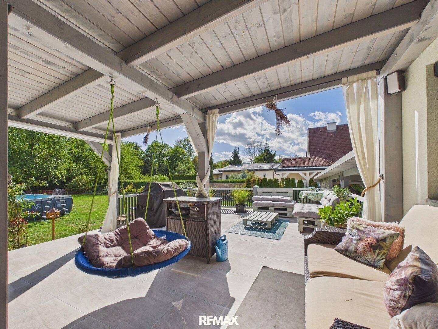 Überdachte Terrasse mit Lounge-Möbeln, Schaukel und Blick auf den Garten und Pool.