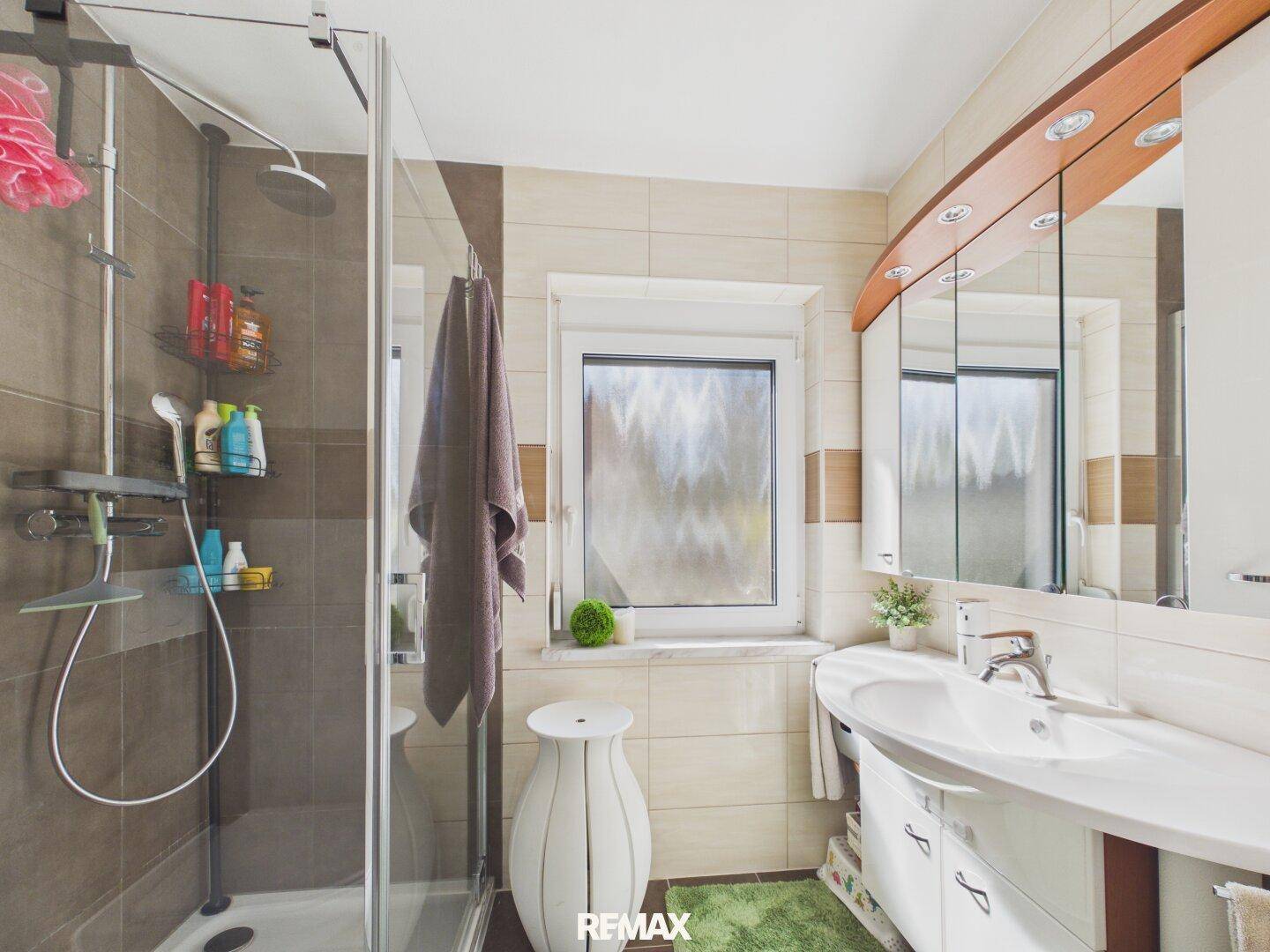 Helles Badezimmer mit Dusche, Waschbecken und Spiegelschrank, modern gefliest.