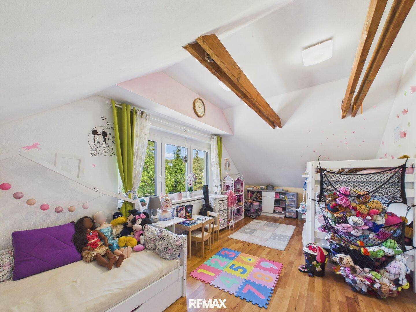 Kinderzimmer mit Holzboden, Dachschräge und Blick auf die grüne Umgebung.