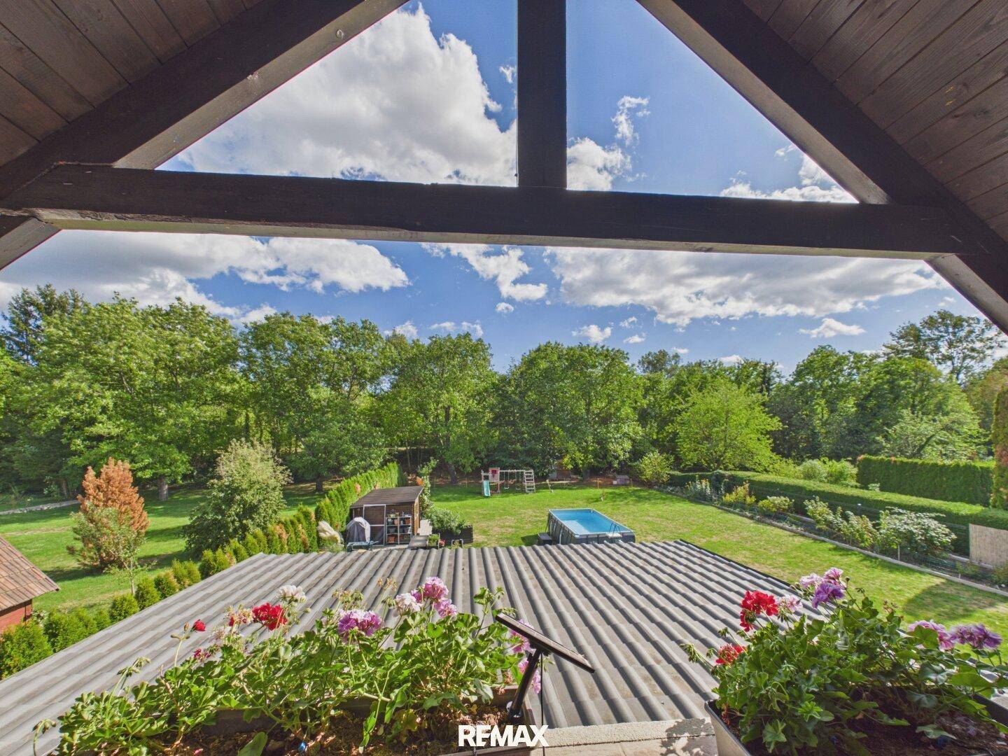 Ausblick vom Balkon über das Dach auf den weitläufigen Garten und die grüne Umgebung.