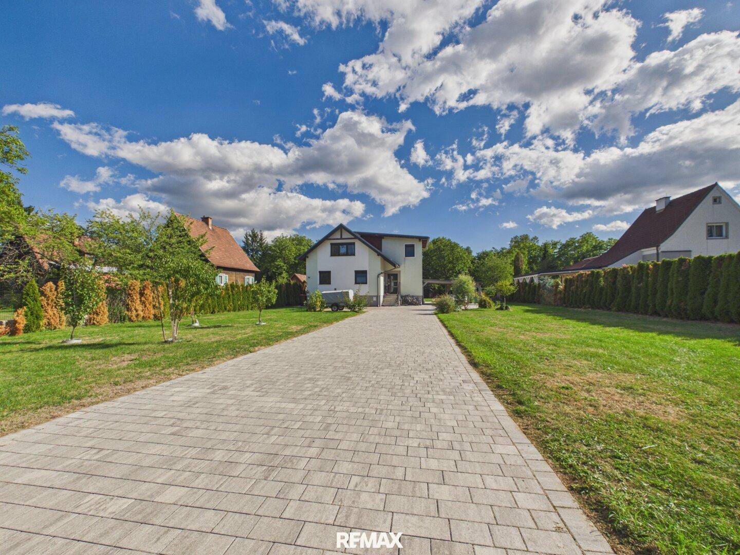 Lange gepflasterte Auffahrt führt zum Haus, umgeben von Rasenflächen und Hecken.