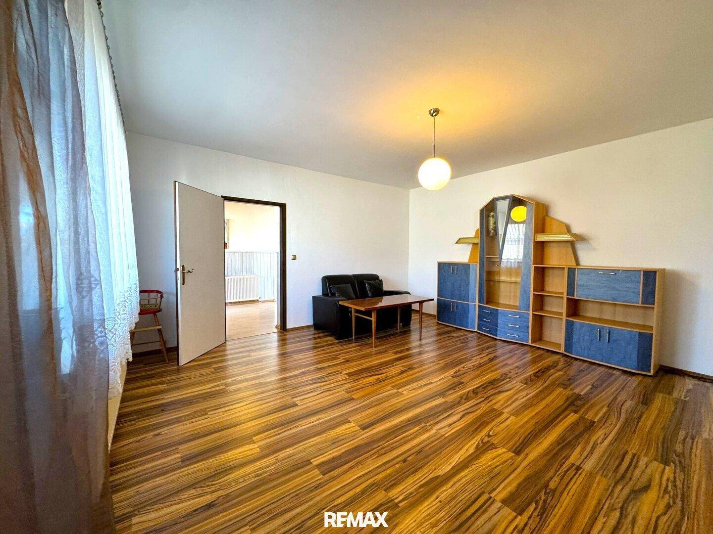 Geräumiges Wohnzimmer mit Laminatboden, dunklem Sofa und einem großen Schrank.