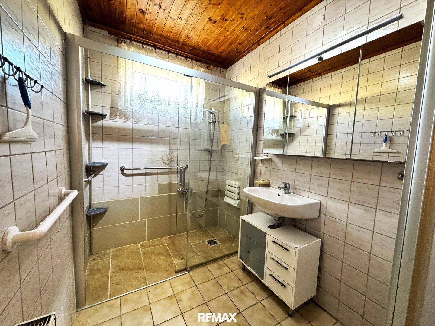 Helles Badezimmer mit Duschkabine, Waschbecken und Holzdecke in Standardausstattung.