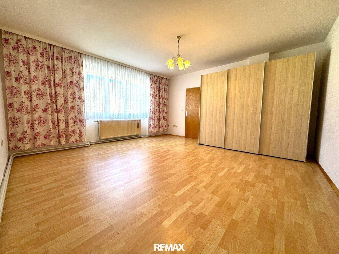 Helles Schlafzimmer mit Holzparkettboden, großem Fenster und Einbauschränken.