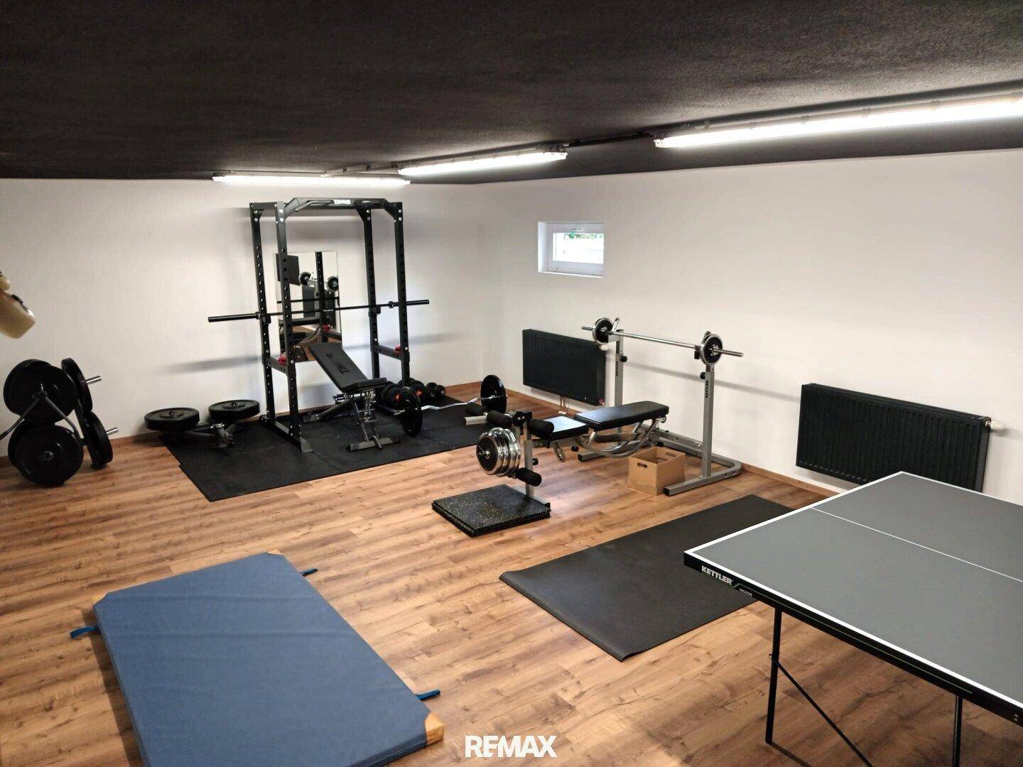 Geräumiger Fitnessraum im Keller mit verschiedenen Trainingsgeräten und Holzboden.