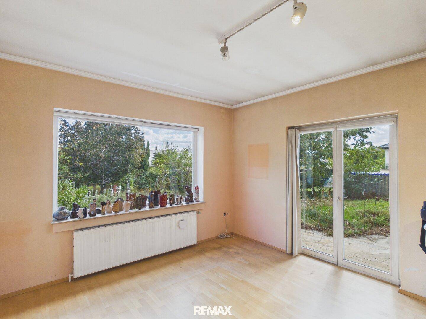Wohnraum mit Parkettboden, großem Fenster und Zugang zur Terrasse oder Garten.