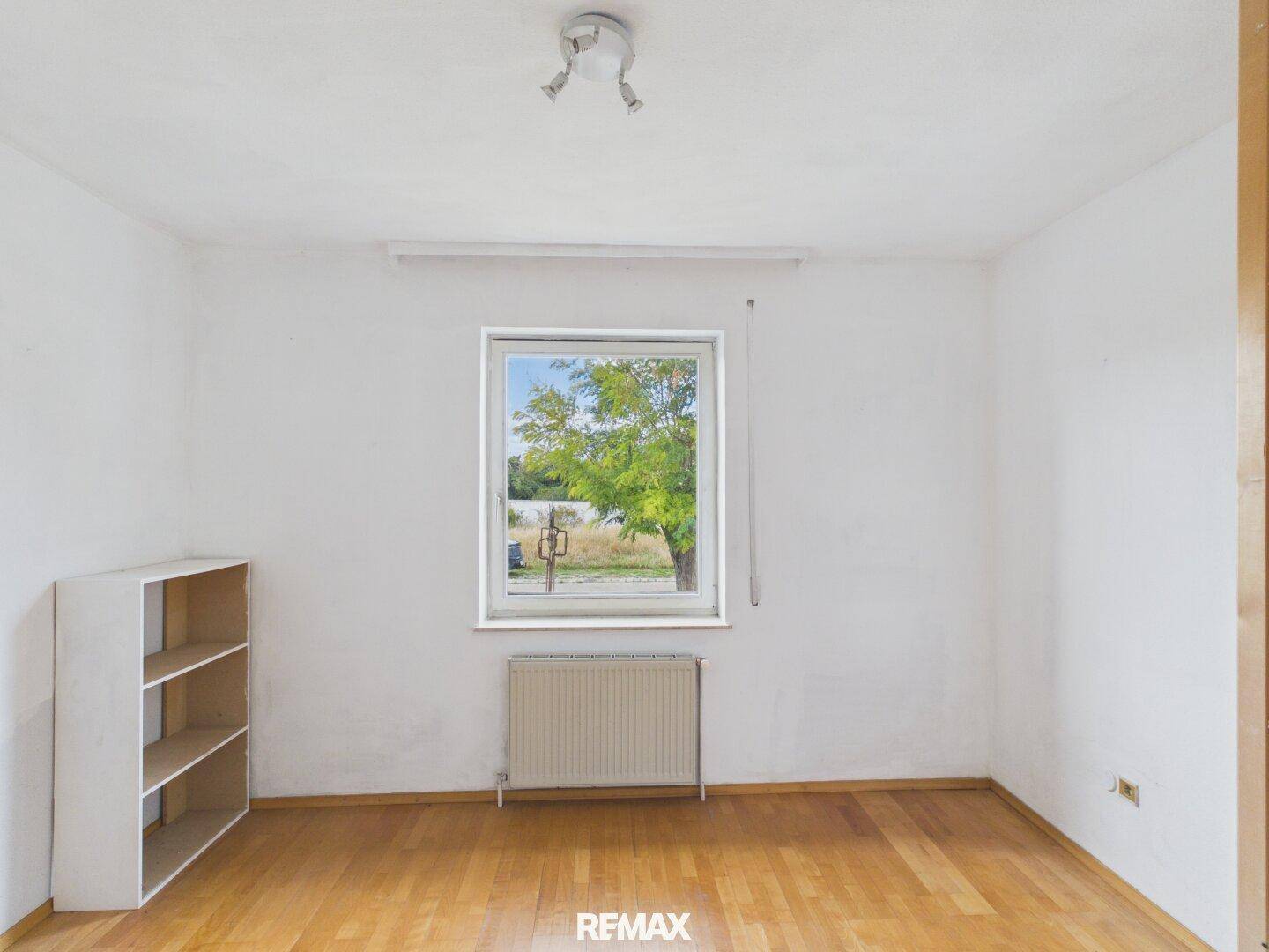 Einfacher Raum mit Parkettboden, Fenster und Heizkörper, ideal als Schlaf- oder Arbeitszimmer.