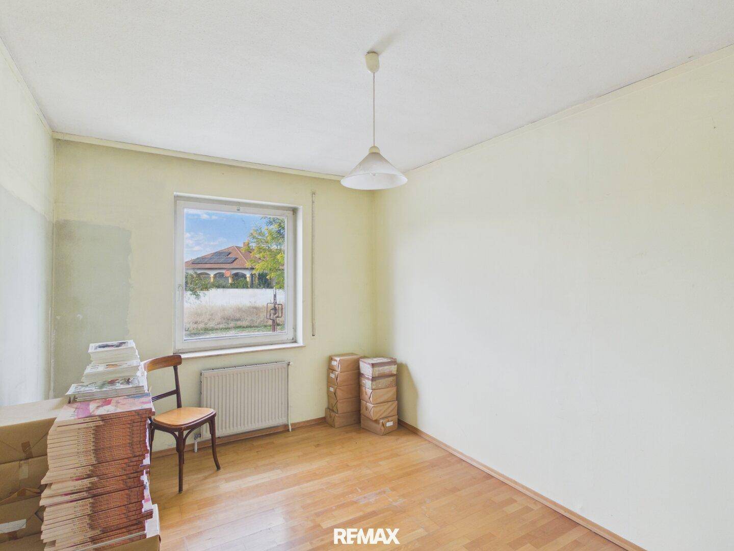 Helles Zimmer mit Parkettboden, Fenster und Heizkörper, mit Blick ins Grüne.