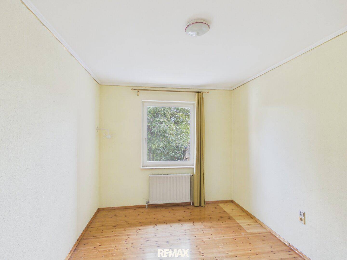 Schlafzimmer mit Holzdielenboden, Fenster und Heizkörper, in einem hellen Ambiente.
