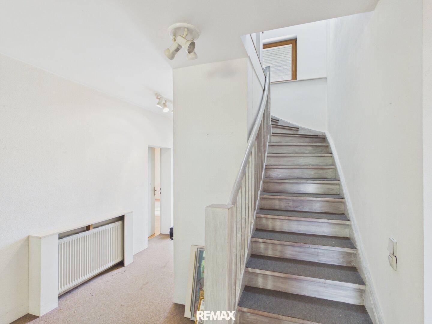 Heller Flur mit Teppichboden und Holztreppe, die in die obere Etage führt.