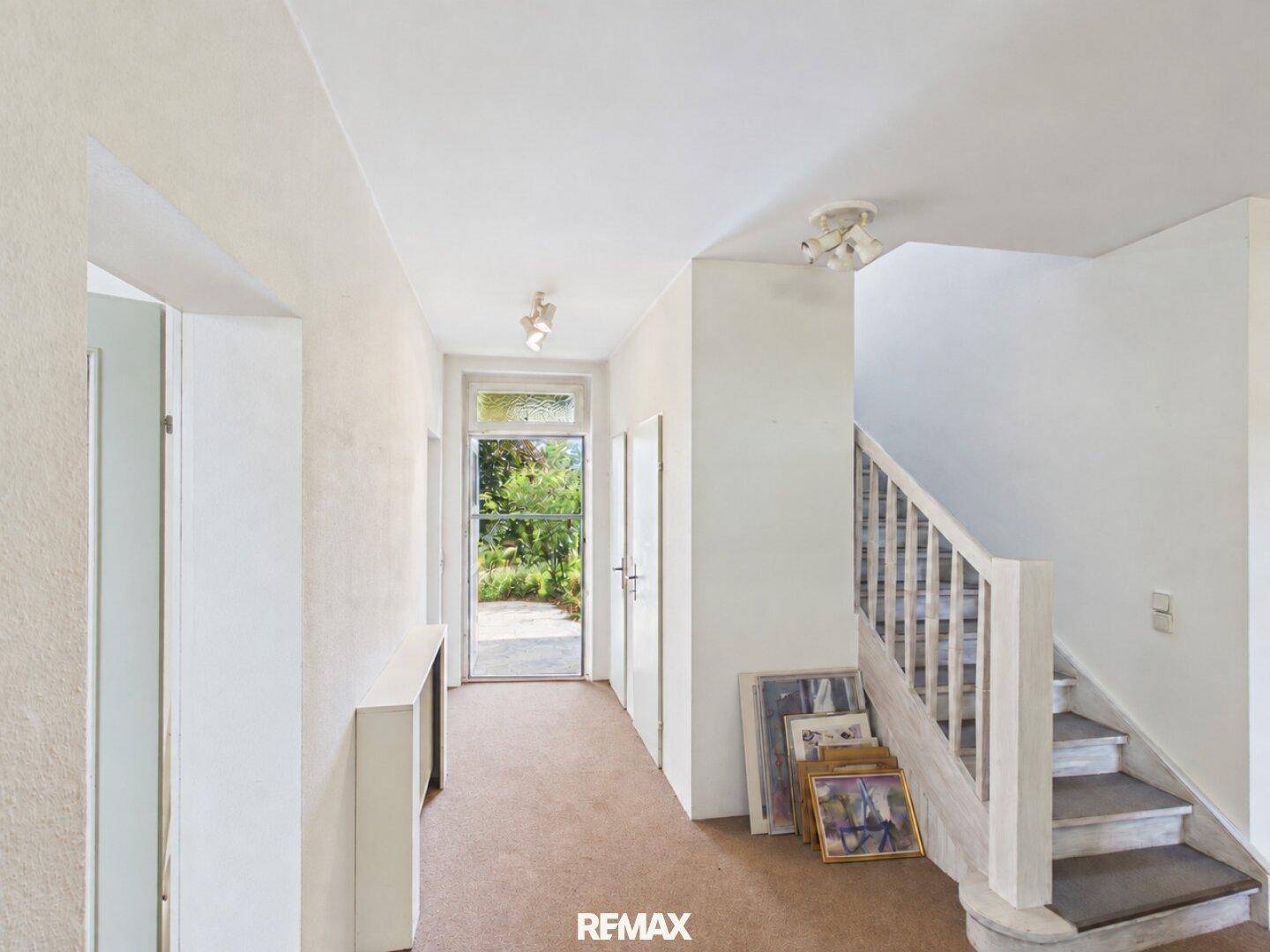 Eingangsbereich mit Teppichboden, Treppe und Blick zum Garten durch die Tür.