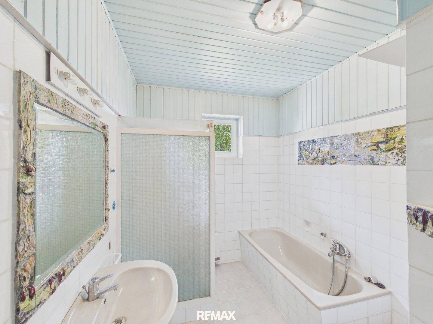 Badezimmer mit weißen Fliesen, Badewanne, Waschbecken und Fenster, im älteren Stil.