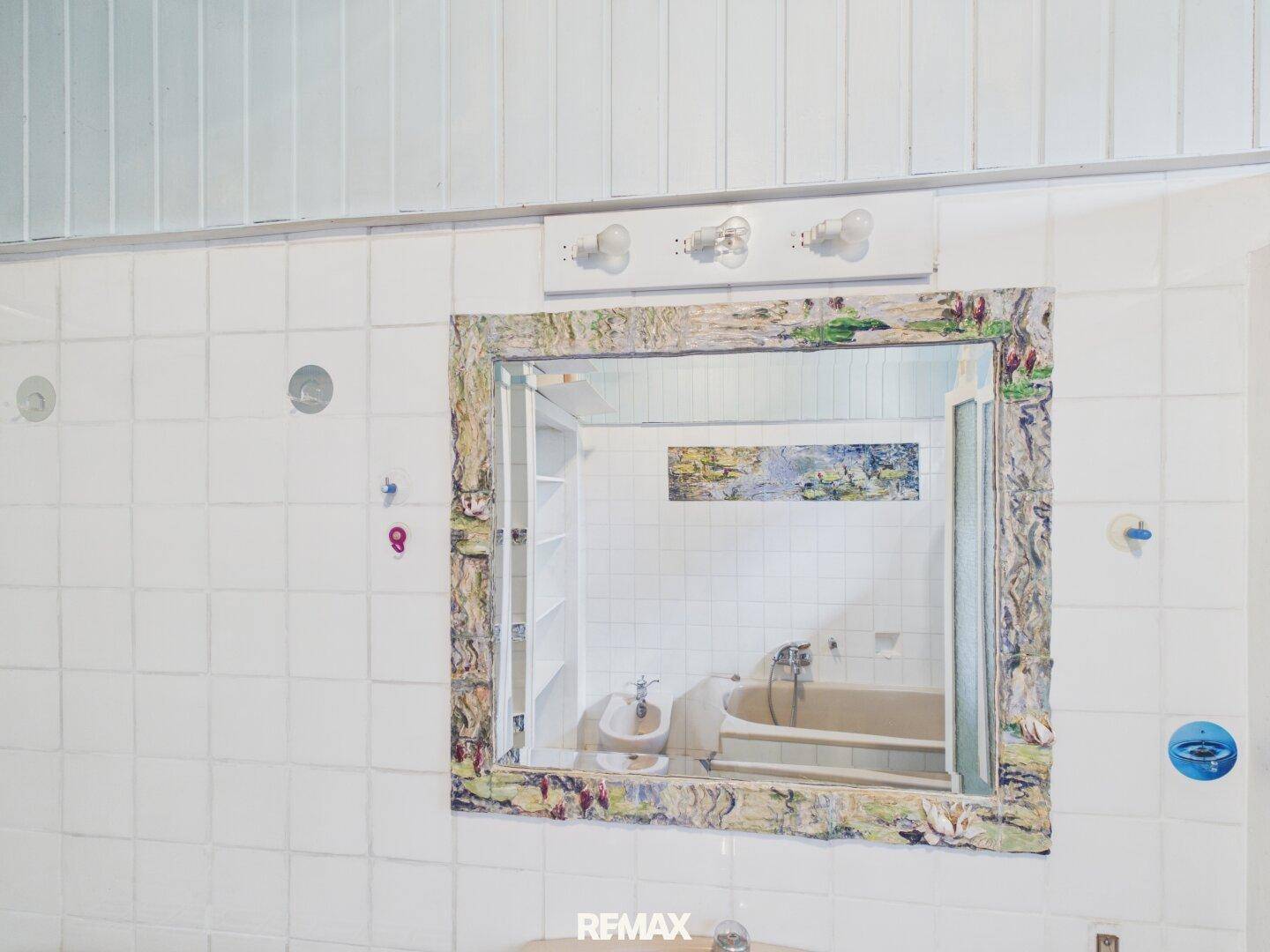 Spiegel im Badezimmer mit dekorativem Rahmen und Blick auf die Badewanne.