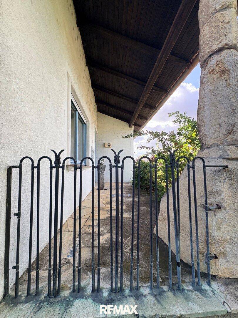 Überdachter Eingangsbereich mit schmiedeeisernem Tor und Steinplattenweg.