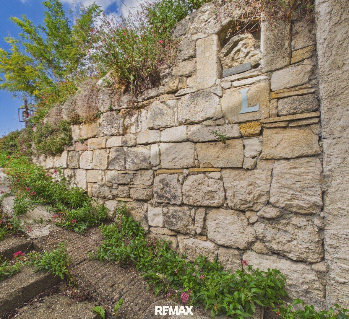 Alte Steinmauer mit Bewuchs und dekorativen Elementen, die das Grundstück begrenzt.