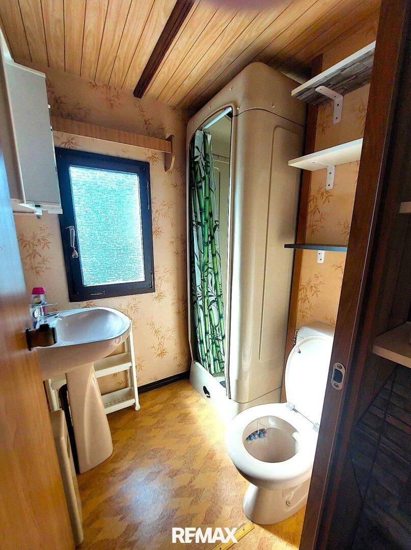 Kleines Badezimmer mit Duschkabine, Waschbecken, Toilette und gemusterter Tapete.