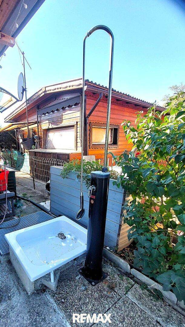 Außendusche und Waschbecken neben einem Holzhaus unter blauem Himmel.