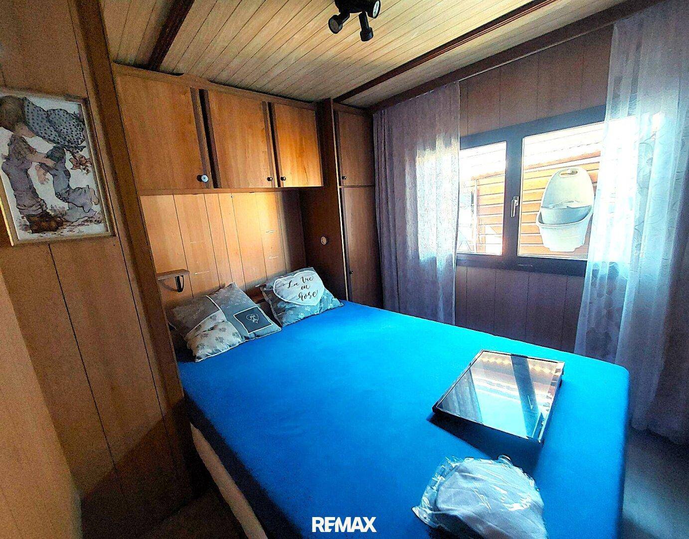 Gemütliches Schlafzimmer mit Holzwänden, Deckenverkleidung und einem Bett mit blauer Decke.