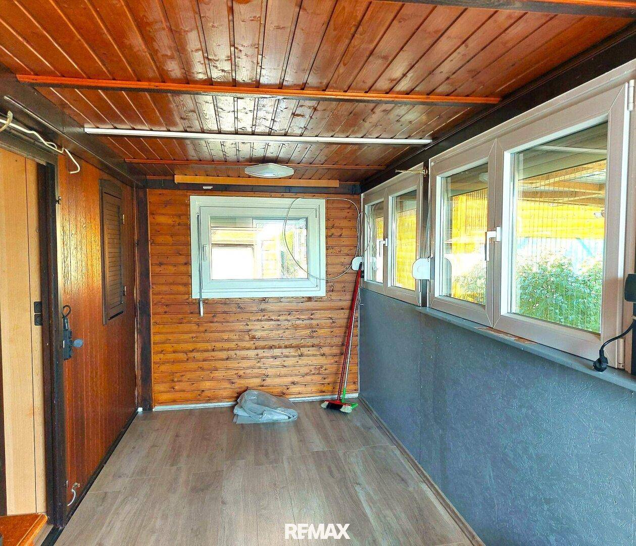 Heller Innenraum mit Holzverkleidung, vielen Fenstern und Laminatboden.